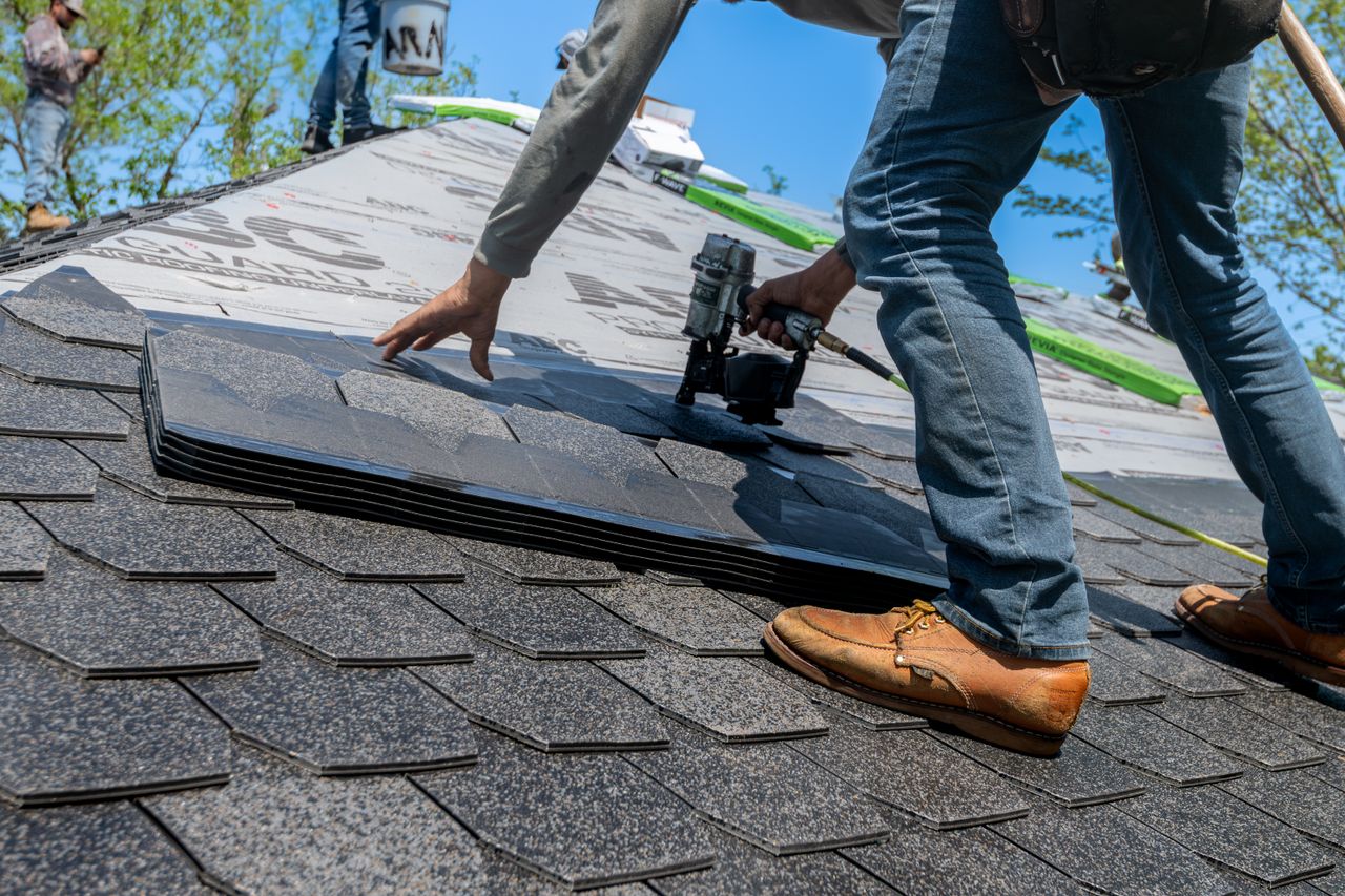 About Roofer using nail gun for shingle installation on residential roof.