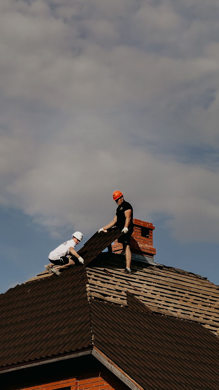 Mastering the First Impression: Your intriguing post title goes here Two workers in safety helmets repair a roof, showcasing outdoor construction during a cloudy day.